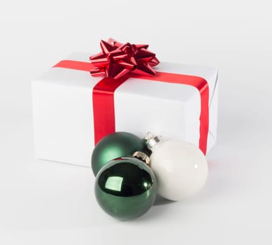 Christmas present in white paper with red ribbon and bow, green and white Christmas balls, isolated on white background