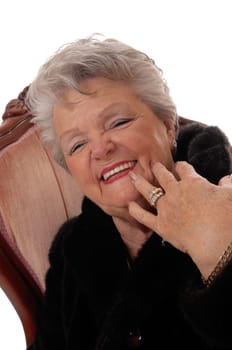 A pretty senior woman in a black fur coat laughing with her mouth open,.sitting in a pink armchair, isolated for white background. .