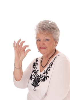 A beautiful senior woman in her seventies holding a vitamin pill, in closeup.isolated for white background..
