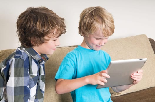 Kid is working on a tablet computer while his brother is watching