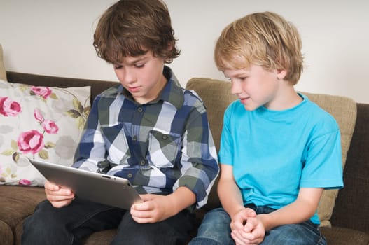 Kid is working on a tablet computer while his brother is watching