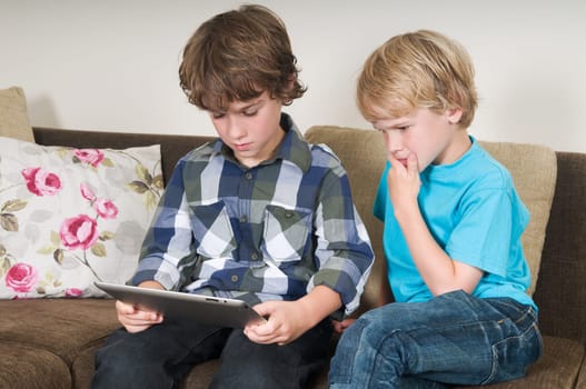 Kid is working on a tablet computer while his brother is watching