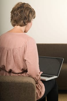 Young woman working at home on a laptop, from behind
