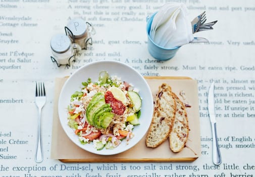 Overhead view of a simple place setting at an eatery consiting of a fresh salad with fresh bread, cutlery, condiments and serviettes