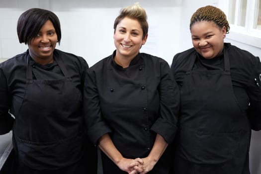 Three chefs standing together and smiling inside bright kitchen