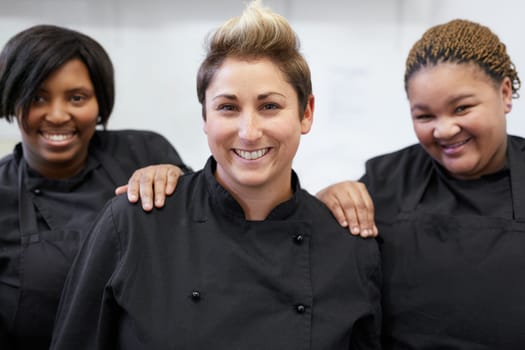 Three chefs standing together inside white kitchen