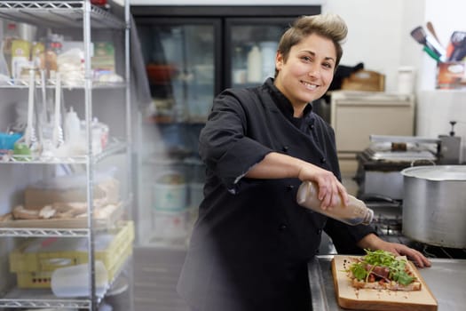 A female chef drizzling balsamic vinegar on an open sandwich