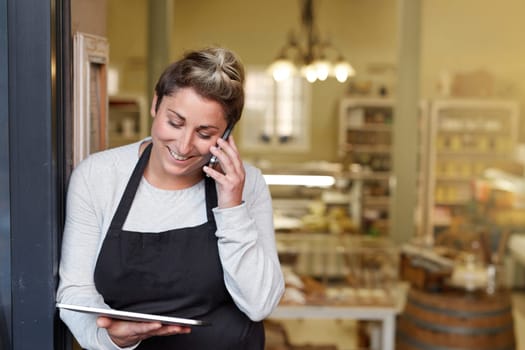 A young deli employee talking on the phone while working on a tablet