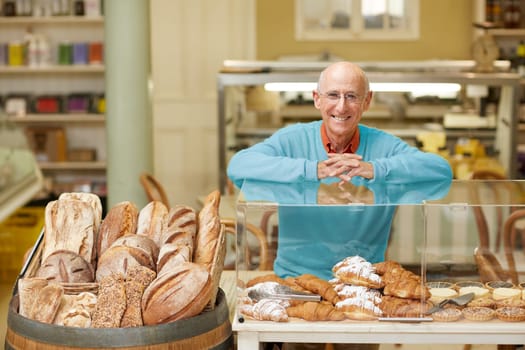 An elderly deli owner standing at the pastry display in his shop