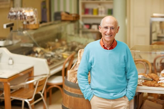 An elderly deli owner standing at the pastry display in his shop