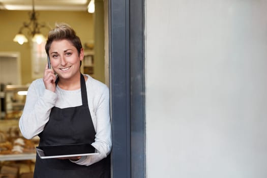 A young deli employee talking on the phone while working on a tablet