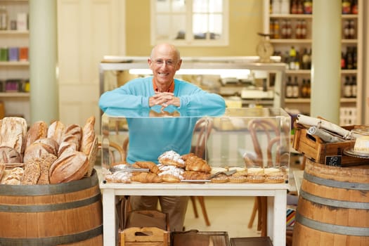 An elderly deli owner standing at the pastry display in his shop