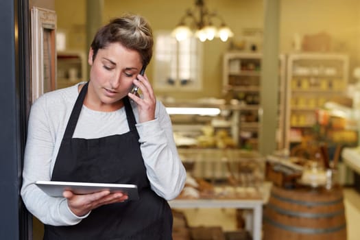 A young deli employee talking on the phone while working on a tablet