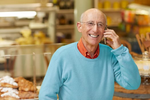 An elderly deli owner talking on the phone in his shop