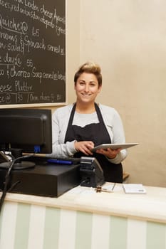 A young deli worker standing behind the counter while working on her tablet