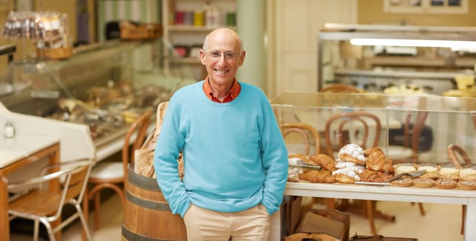 An elderly deli owner standing at the pastry display in his shop