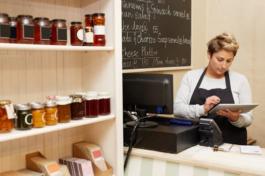 A young deli worker standing behind the counter while working on her tablet