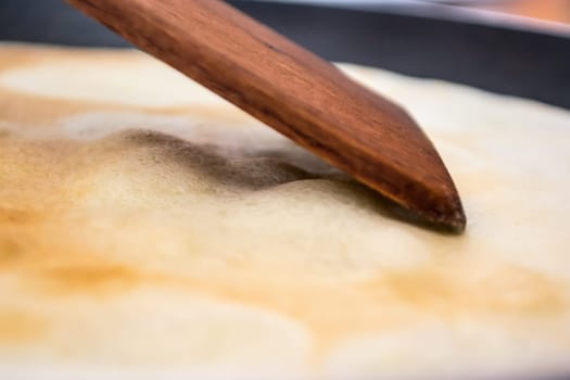 Wooden mixing spoon touching pancake while been backed
