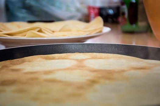 Baking pancakes with stack of pancakes in the background