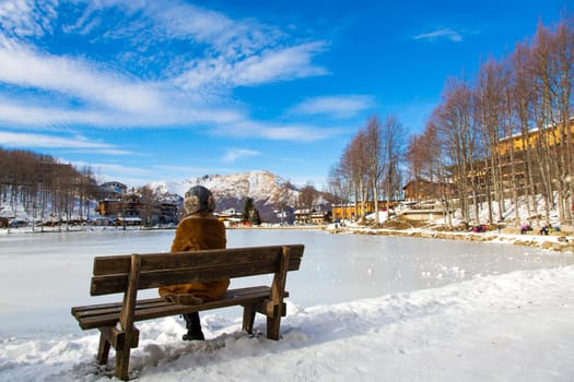 View from behind of a woman sitting on a bench in a Tuscan snowy landscape