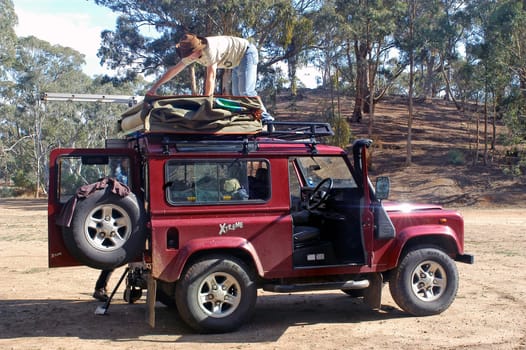 A camper fold his tent on the roof of his car in the forest where he has spent the night