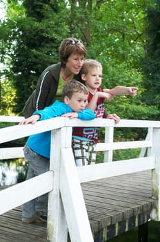 Grandma is standing on a bridge with her two grandsons, looking at a lake.