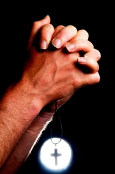 Praying hands holding a cross in front of a bright light.