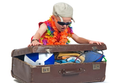 Little boy trying to fit all his stuff for the summer vacation in his suitcase.