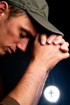 Praying man holding a cross in front of a bright light.