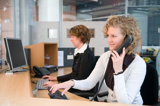 Two professional women working at a front desk.