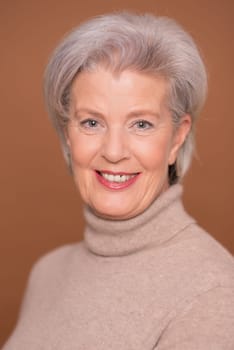 Studio recording of a smiling older woman against a brown background