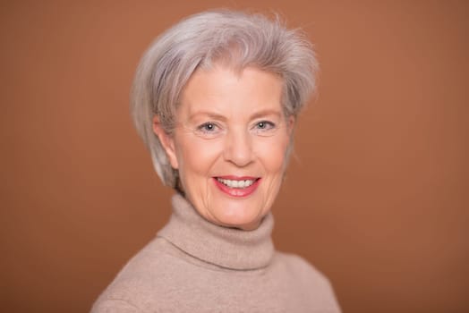 Studio recording of a smiling older woman against a brown background