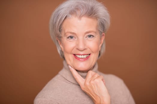 Studio recording of a smiling older woman against a brown background