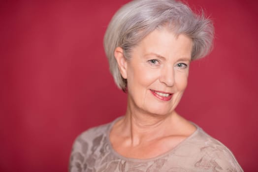 Studio recording of an older woman against a red background