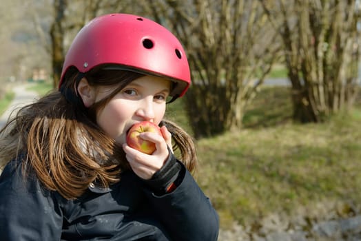 a preteen in roller skate, eat an apple on the side of the road