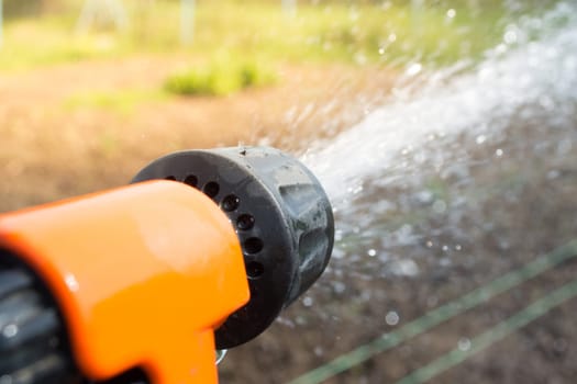 Closeup of hand held sprinkler with water spraying on the field