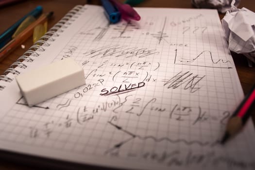 Notebook full of written formulas with pencil and eraser on top of it. Crumpled paper all around the table