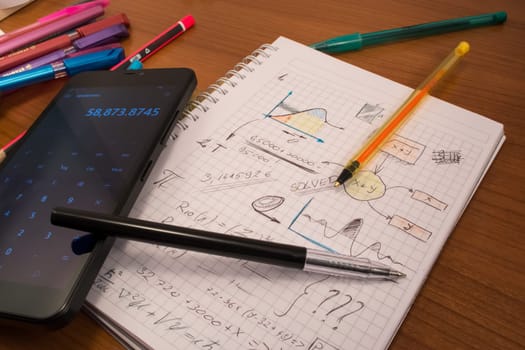Notebook full of mathematics. Smart phone and pencils are visible