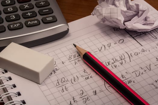 Messy table with notebook, pencils, crumpled papers and calculator