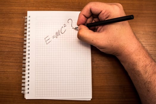 Hand with pencil and notebook. Hand written formula for transforming mass in to a energy