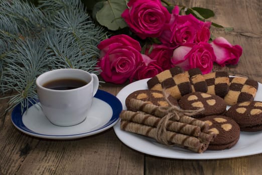 cup of coffee, roses and plate with different cookies on a table
