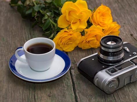 bouquet of yellow roses, cup of coffee and a retro the camera on a table