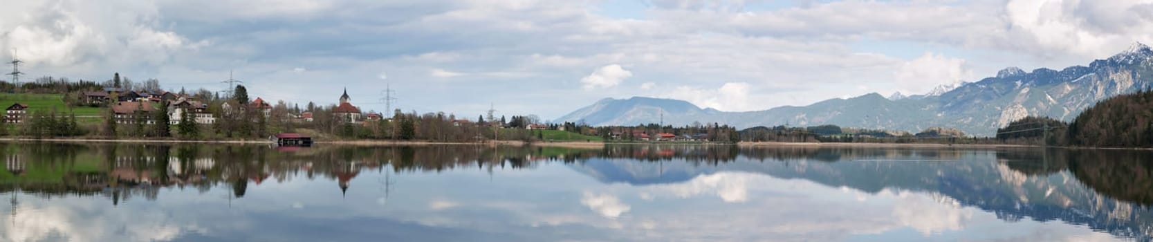 north-eastern panoramic view over the Weissensee near the town of Füssen in the Ostalgäu with beautiful water reflection and the village of Weissensee as well as snow-capped mountains in the background