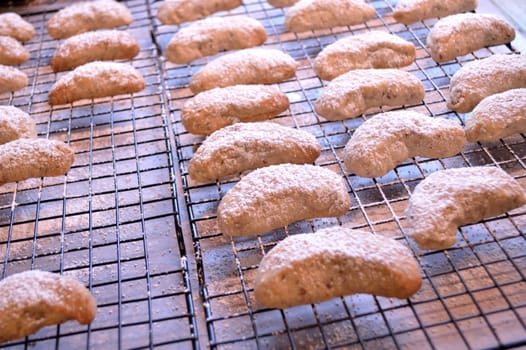 Crescent cookies, fresh out of the oven, and layed out on cooling racks to cool. Powdered sugar sprinkled on top.