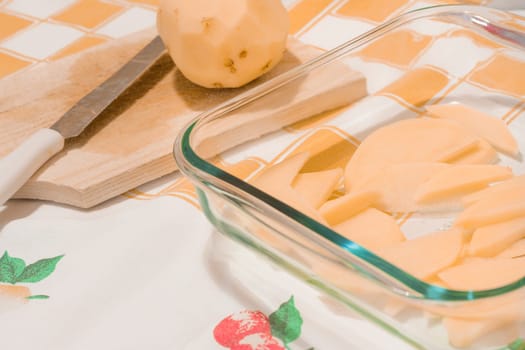 Sliced potatoes in a glass tray on a kitchen table