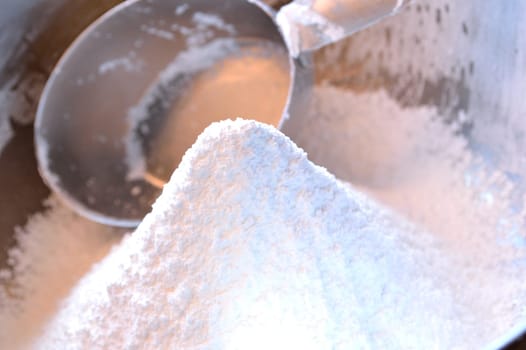 Closeup photo of a mound of freshly sifted confectioner's sugar in stainless steel bowl with 1 cup measuring cup in background.