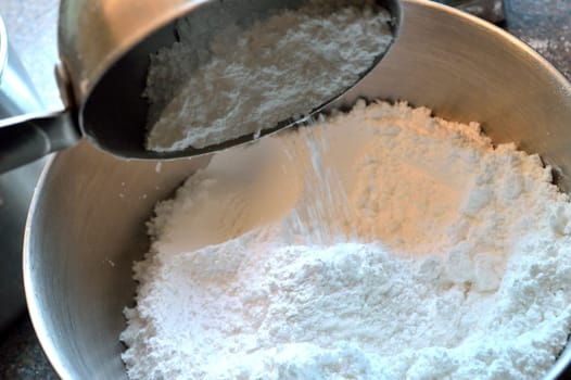 Pouring one cup of sifted powdered sugar into a stainless steel bowl. Baking action photo of baker measuring ingredients.