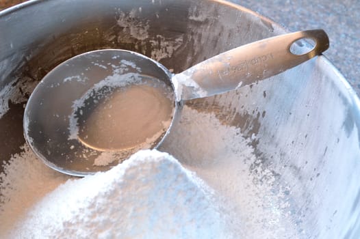 Closeup photo of a stainless steel measuring cup in a bowl of confectioner's sugar, freshly sifted.