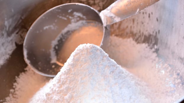 Closeup panorama photo of a mound of freshly sifted confectioner's sugar in stainless steel bowl with 1 cup measuring cup in background.