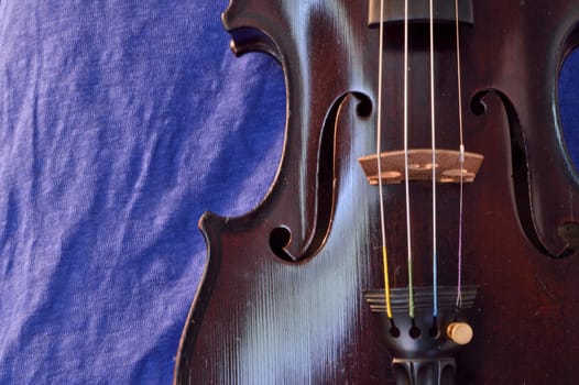 Closeup of violin against a blue linen background. Violin is an antique from the early 1800's in a dark stain (original finish).